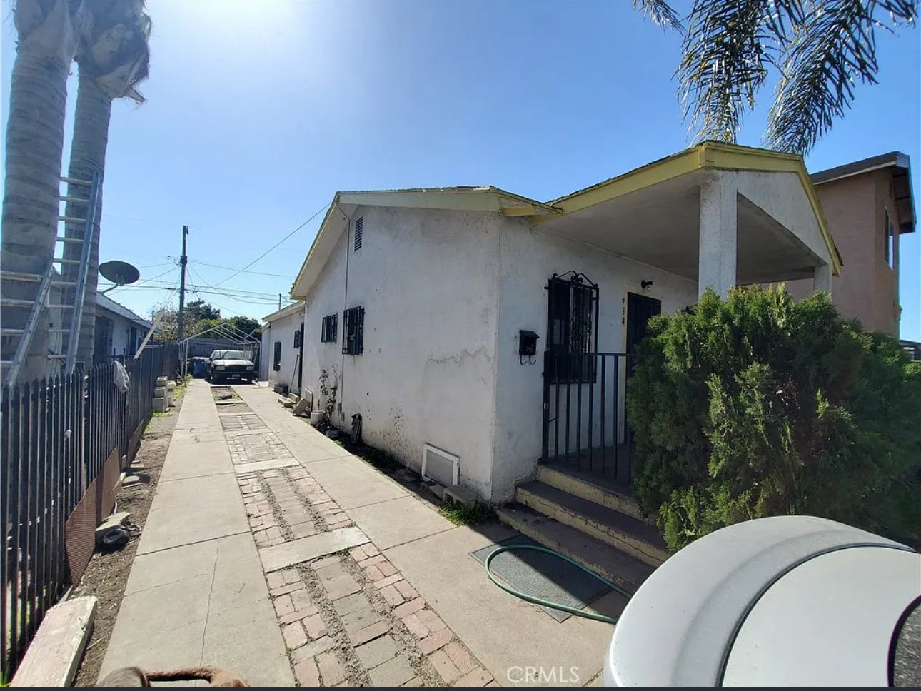 A single-story white house small front porch, and barred windows in Los Angeles